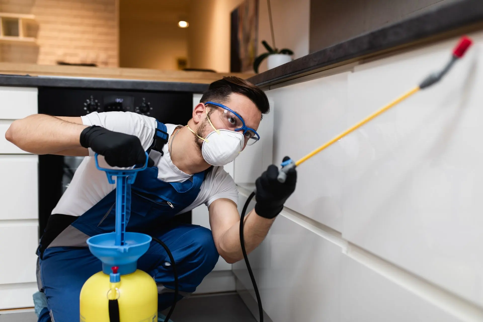 Exterminator in a respirator spraying insecticide inside a modern kitchen